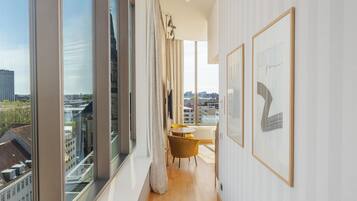 A modern hotel room with large windows, a wooden floor, and a dining area with yellow chairs.