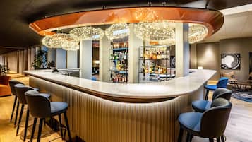 Una zona de bar moderna con una barra curva, taburetes y luces decorativas colgantes.
