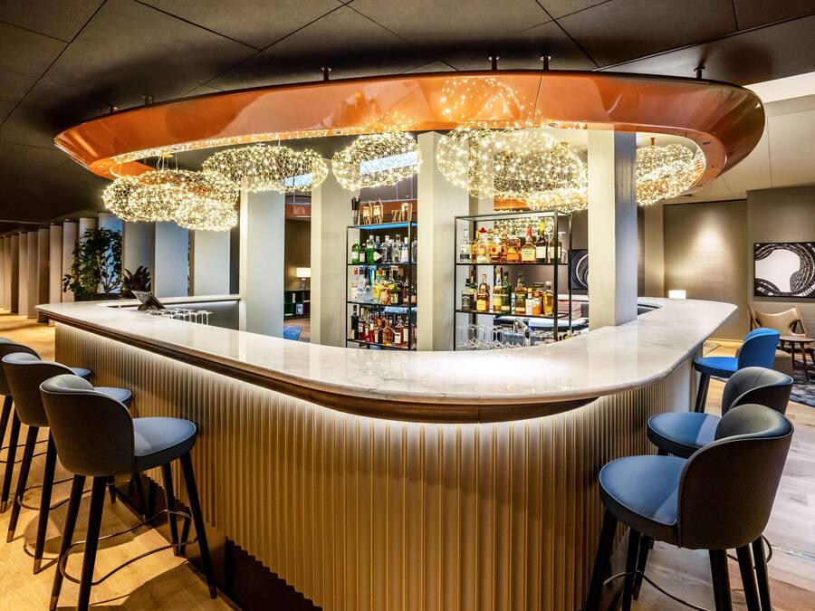 A modern bar area with a curved counter, bar stools, and overhead decorative lighting.