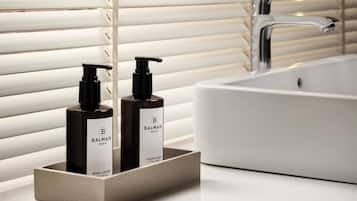 A bathroom with a white sink, two bottles of Balmain body lotion, and a modern faucet.