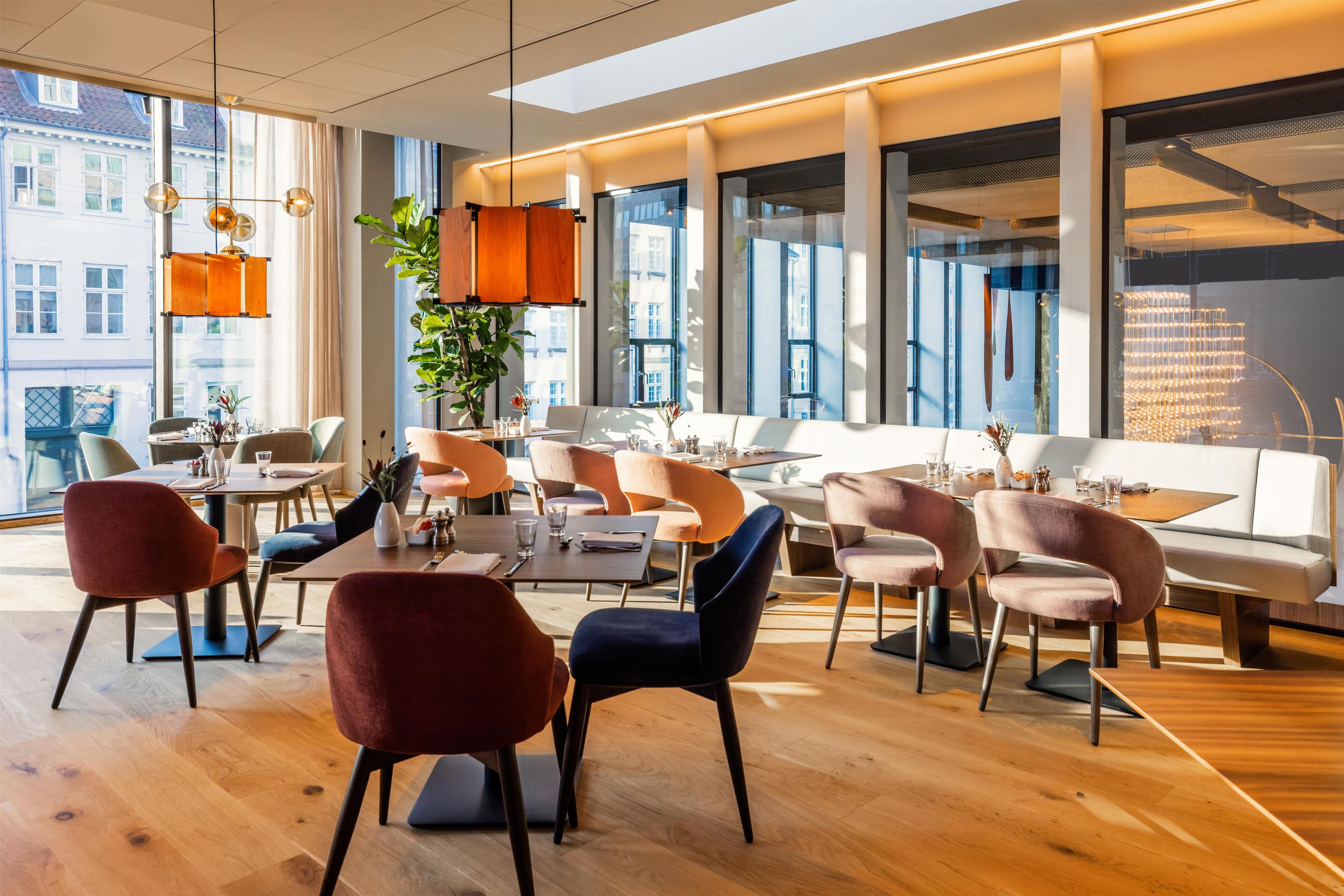 Een moderne eetruimte met houten vloeren, diverse zithoeken en grote ramen met uitzicht op de stad.