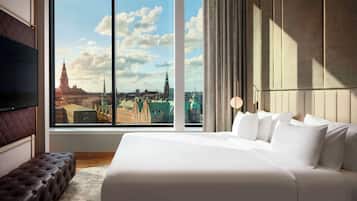 A modern hotel room with a large window offering a cityscape view, a plush bed, and a seating area.