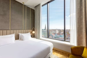 Una habitación de hotel con una cama grande, vistas a la ciudad y un diseño moderno.