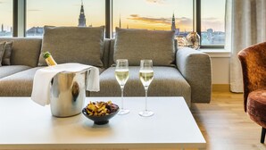 A modern living room with a sofa, a table with a bottle and glasses, and a bowl of snacks. - NH Collection Copenhagen (Copenhagen)