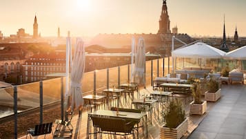 A rooftop terrace with outdoor seating, a view of the city skyline, and a sunset.