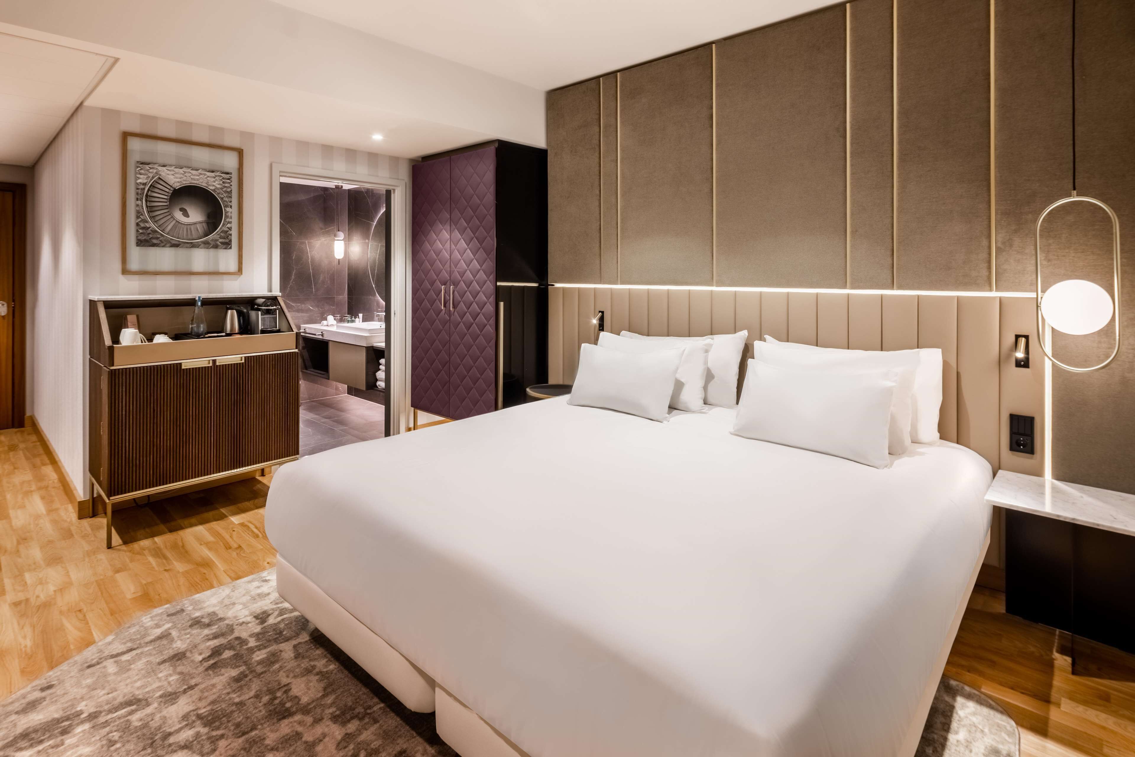 A modern hotel room with a large bed, a vanity with a mirror, and a built-in wardrobe.