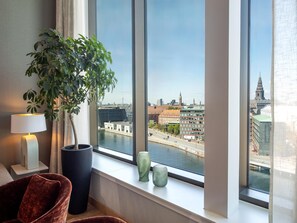 Una habitación con un ventanal grande, una planta en maceta, una lámpara y una silla.