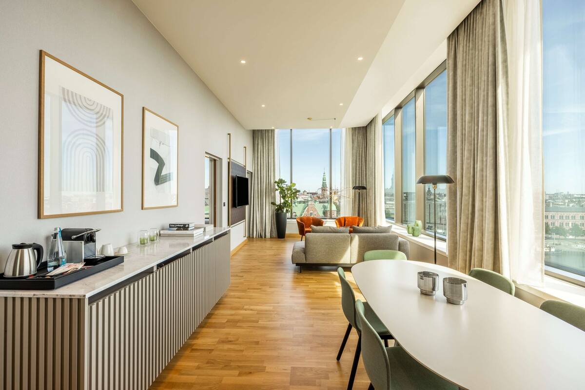Una habitación de hotel moderna con una encimera de cocina amplia, zona de comedor y grandes ventanales con vistas a la ciudad.
