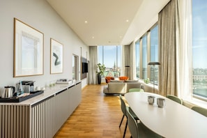 Una habitación de hotel moderna con una encimera de cocina amplia, zona de comedor y grandes ventanales con vistas a la ciudad.