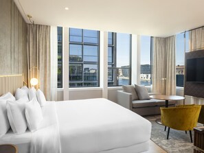 Una habitación de hotel moderna con una cama grande, un sofá, una mesita y un televisor.