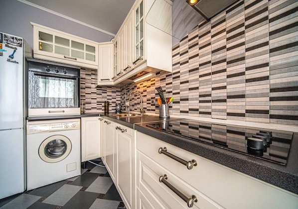 Compact kitchen with oven, washing machine, and geometric-patterned backsplash.