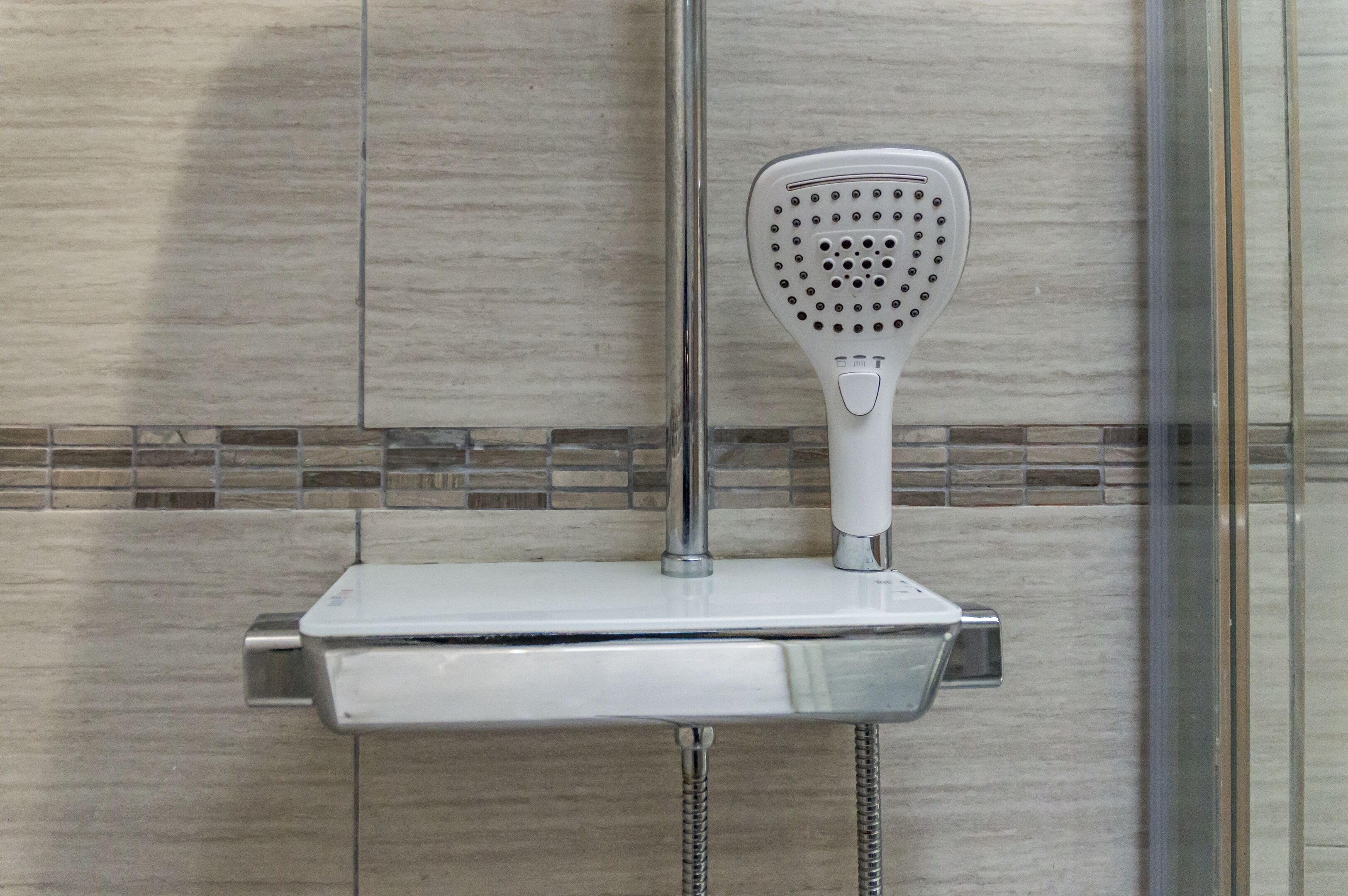 A shower with a handheld showerhead mounted on a wall-mounted control panel.