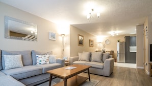 A modern living room with a sofa set, a wooden coffee table, and a dining area with a chandelier.