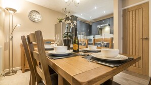 A dining area with a wooden table set for four, including plates, bowls, cutlery, and a bottle of wine.