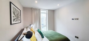 Cozy retreat with a large window, a neatly made bed, and a floor lamp for added lighting.