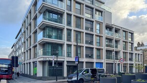 A modern multi-story building with large windows and balconies, a visible street sign, and a speed limit sign. - Two Bed Serviced Apt in Old Street (London)