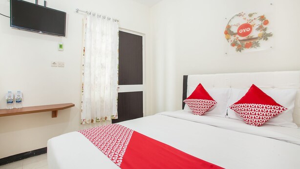 Een hotelkamer met een bed, een aan de muur bevestigde televisie, een plank met waterflessen en een decoratief wandobject.