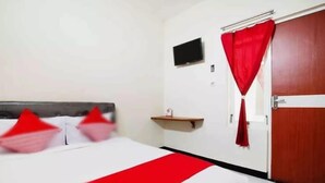 Een hotelkamer met een bed, een aan de muur bevestigde televisie en een deur met een rood gordijn.