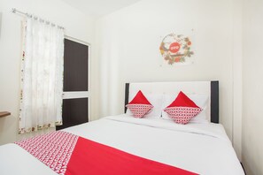 A hotel room with a bed, a window with curtains, a wall decoration, and a door. - OYO 3350 Cozy Residence Syariah (Malang)