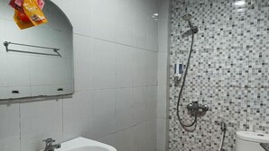 Een badkamer met een wastafel, een douche met een betegelde muur in mozaïek en een toilet.