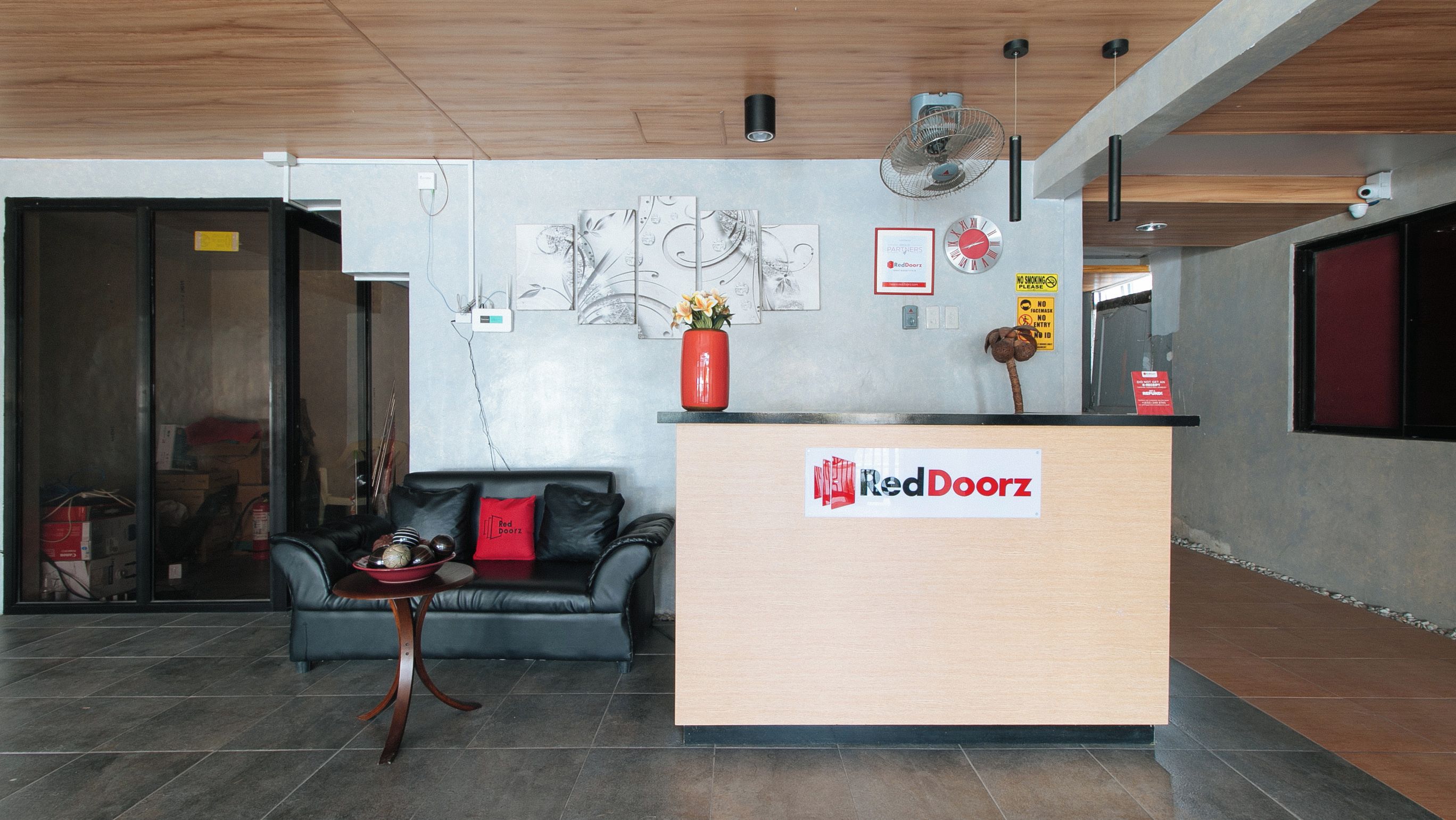 Ein Empfangsbereich mit einer Rezeption, einer schwarzen Ledersofa, einer Blumenvase und Wandbildern.