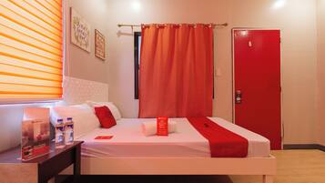 Une chambre d’hôtel avec un lit, une table de chevet, une porte rouge et une fenêtre avec des stores.