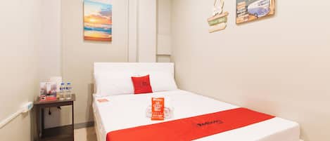 Habitación de hotel con cama, mesita de noche, botella de agua, antifaz RedDoorz y un cuadro de atardecer en la pared, junto con dos letreros RedDoorz.