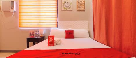 Una habitación de hotel con una cama, una mesita de noche, una ventana con persianas, una pared con dos letreros y una cortina roja.
