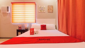 Hotelkamer met een bed, nachtkastje, raam met jaloezieën, muur met twee borden en een rood gordijn.