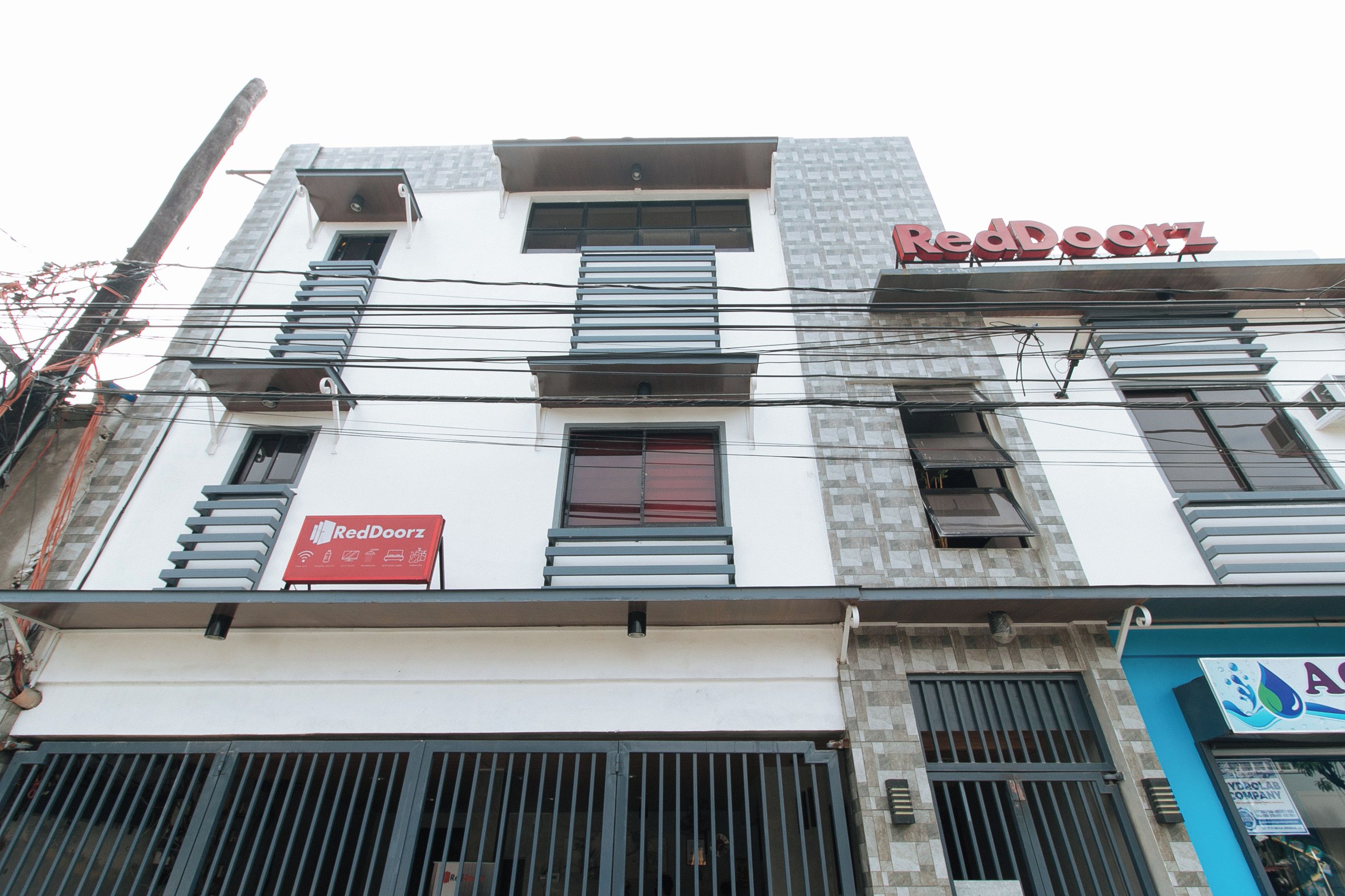 A multi-story building with a RedDoorz sign, a visible storefront with a blue awning, and a large metal gate at the entrance.