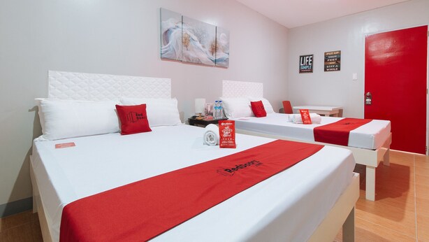 Een hotelkamer met twee bedden, wit beddengoed, rode accenten, een schilderij aan de muur en motiverende posters.