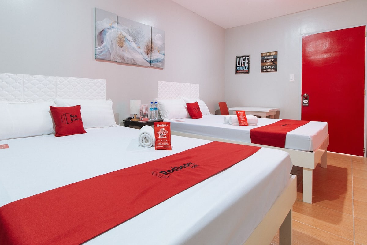 Een hotelkamer met twee bedden, wit beddengoed, rode accenten, een schilderij aan de muur en motiverende posters.
