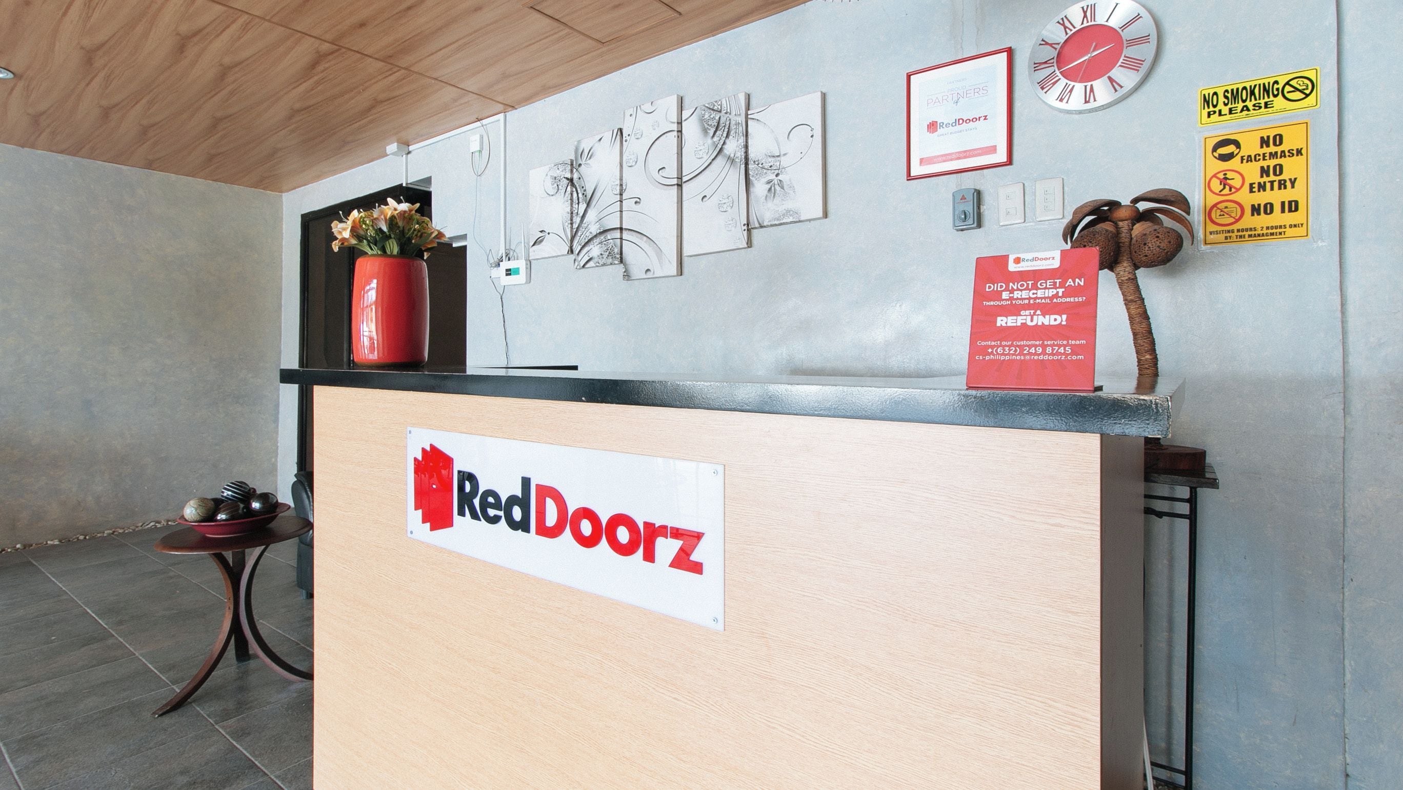Una reception con il cartello RedDoorz, una sveglia e il segnale di divieto di fumo.