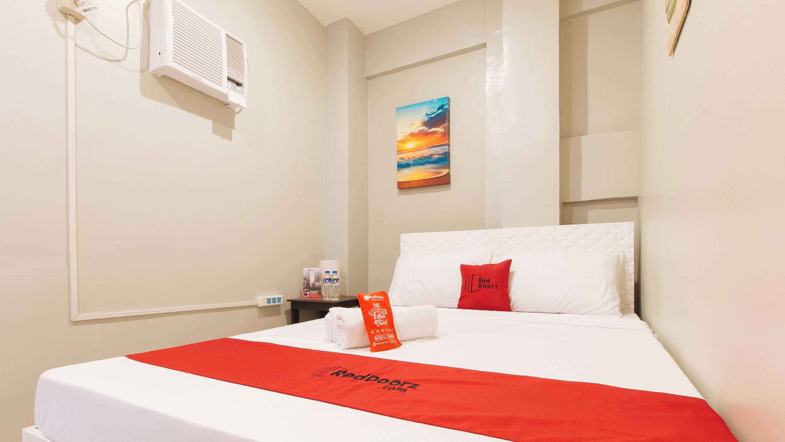 Une chambre d’hôtel avec un lit, un tableau accroché au mur et une couvre-lit rouge et blanche.