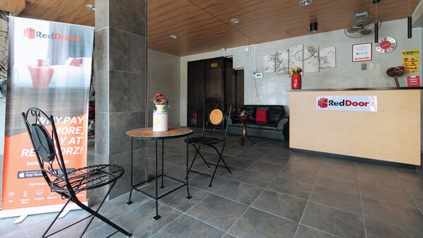 Un espace d'accueil avec une enseigne RedDoorz, un comptoir de réception, une horloge et un mur décoré d'œuvres d'art.