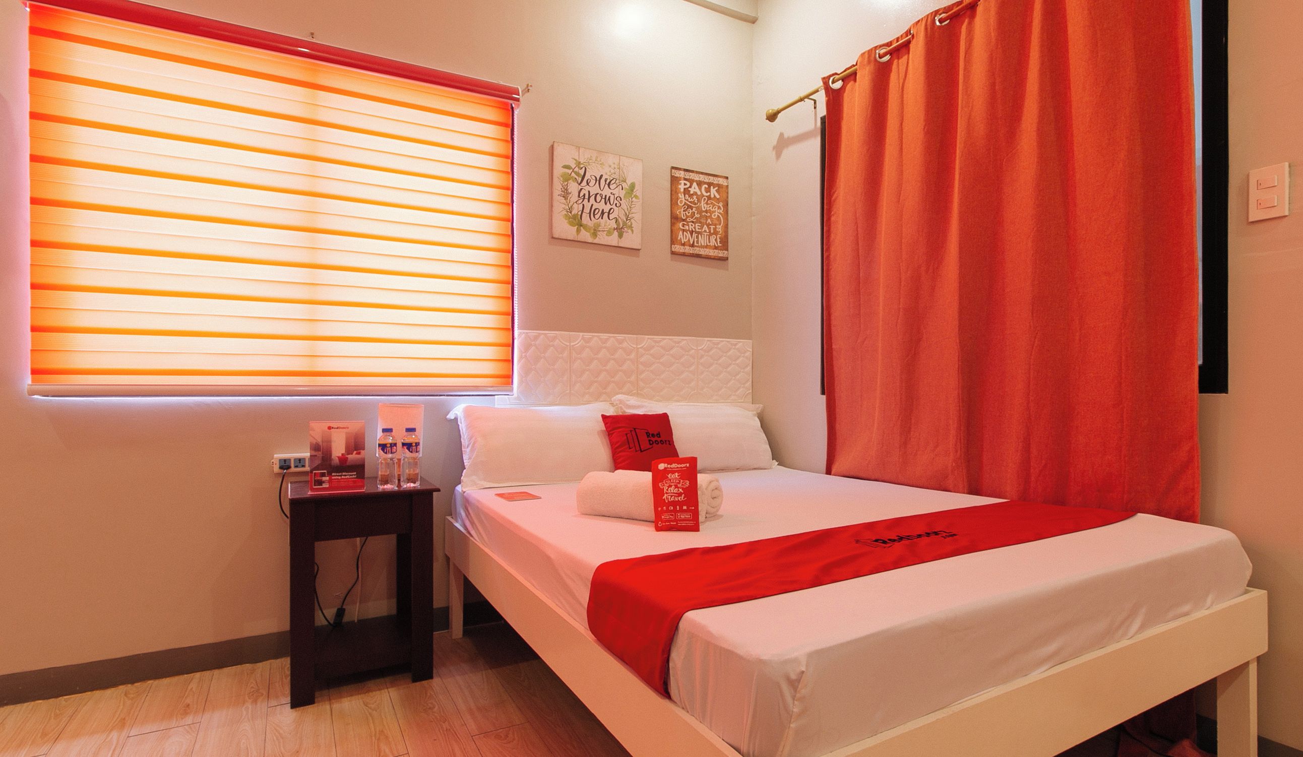 A hotel room with a bed, a nightstand, a window with blinds, and a wall with two signs.