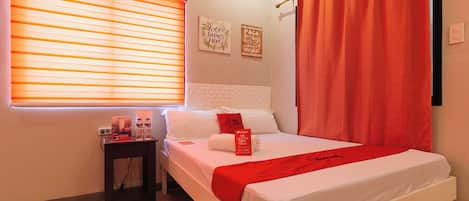 A hotel room with a bed, a nightstand, a window with blinds, and a wall with two signs.