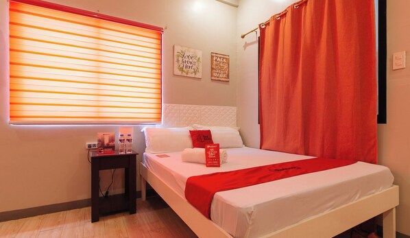 A hotel room with a bed, a nightstand, a window with blinds, and a wall with two signs. - Reddoorz Near Christ the King Medical Center (Las Pinas)