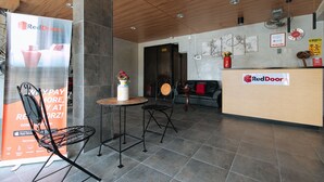 Een ontvangsthal met een RedDoorz bord, een receptiebalie, een ronde tafel met een vaas, en een zwarte stoel.