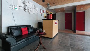 A reception area with a black leather sofa, a small wooden table, and a reception desk with a red door in the background.