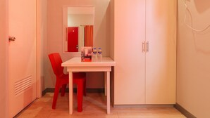 Een kleine kamer met een witte tafel, een rode stoel en een garderobe. Er staan twee flessen op de tafel.