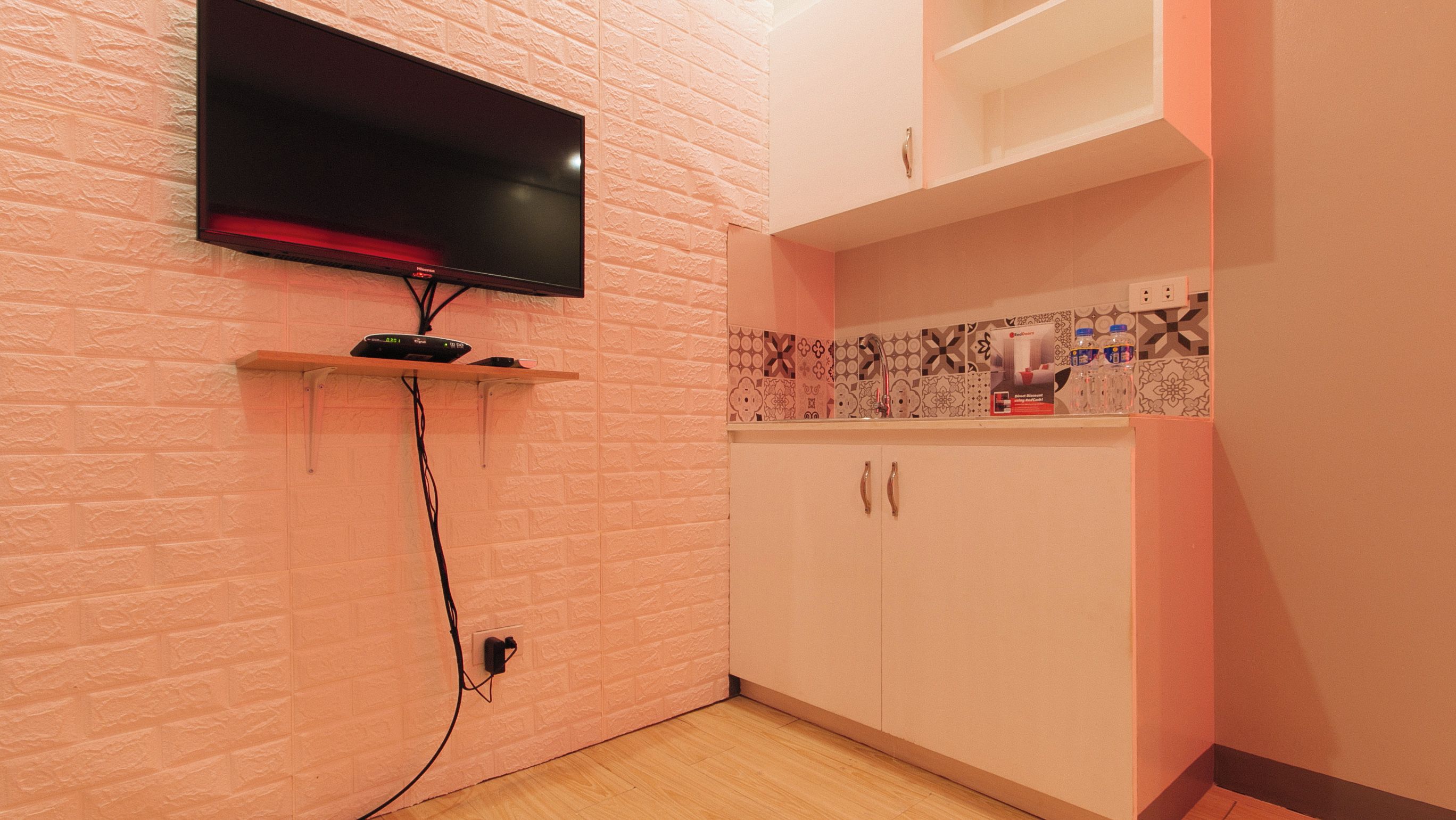 Ein Zimmer mit einem an der Wand befestigten Fernseher, einem Regal mit elektronischen Geräten, einer gemusterten Spritzschutzleiste und einem weißen Schrank.