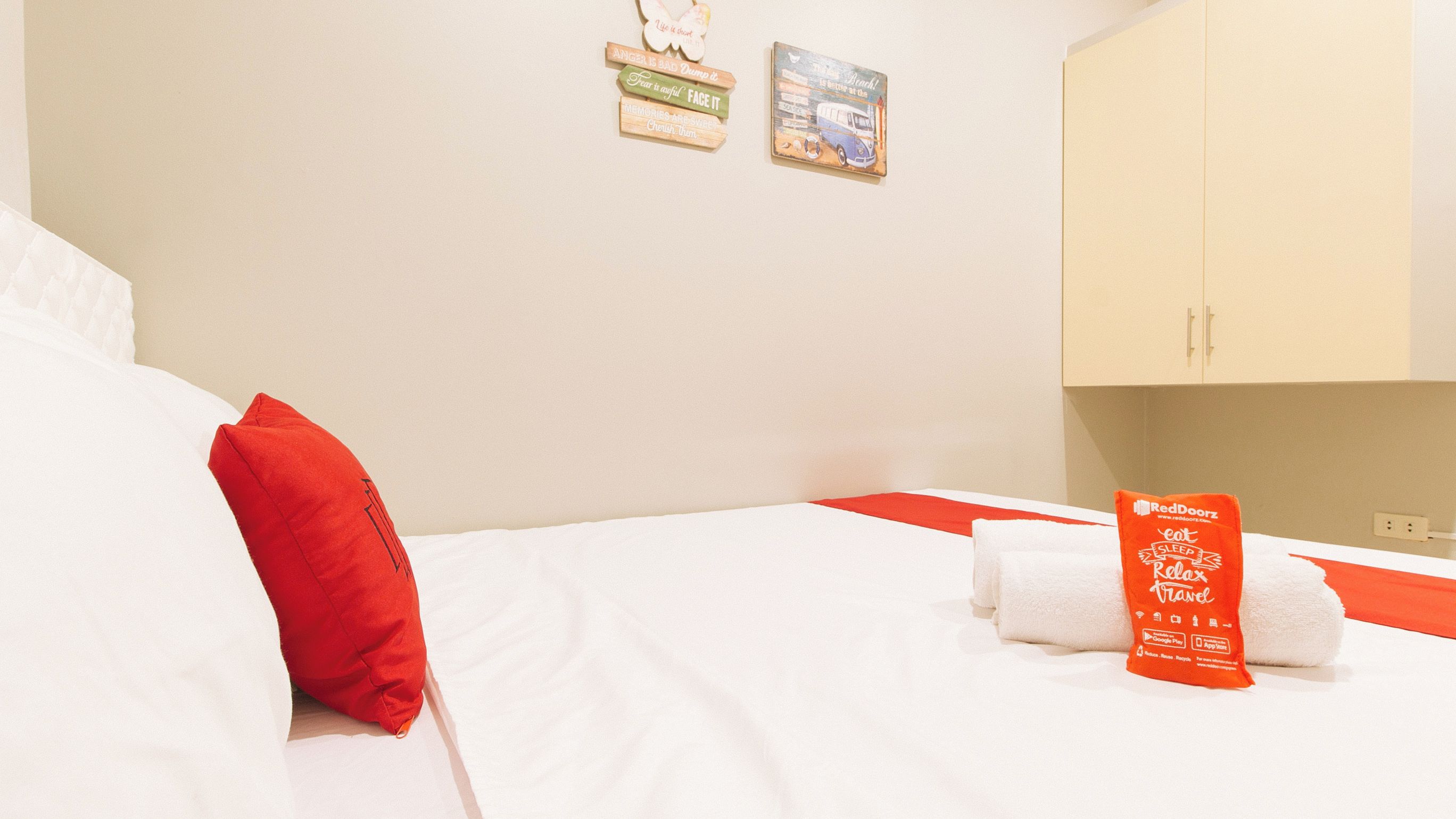 A hotel room with a bed, a red pillow, white towels, and a RedDoorz sign.