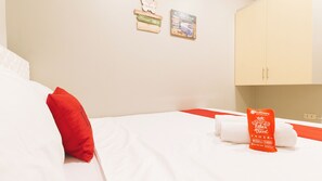A hotel room with a bed, a red pillow, white towels, and a RedDoorz sign.