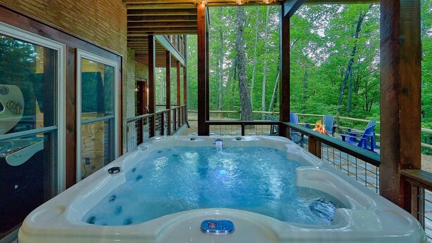 A hot tub in a wooden deck area with a view of a forest. - Luxury Pool Cabin w Theater | Firepit | Hot tub (Sevierville)