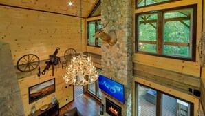 A spacious interior with a stone fireplace, a mounted deer head, and a chandelier. - Luxury Pool Cabin w Theater | Firepit | Hot tub (Sevierville)