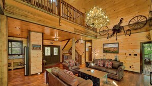 A spacious wooden interior with a staircase, leather sofas, a chandelier, and rustic decor. - Luxury Pool Cabin w Theater | Firepit | Hot tub (Sevierville)