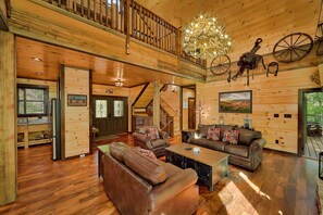 A spacious wooden interior with a staircase, leather sofas, a chandelier, and rustic decor. - Luxury Pool Cabin w Theater | Firepit | Hot tub (Sevierville)