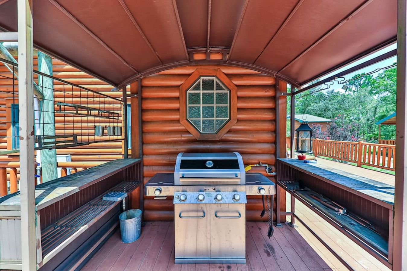 Une cabane en rondins avec un barbecue au centre, des bancs en bois et une fenêtre.