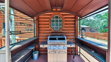 Une cabane en rondins avec un barbecue au centre, des bancs en bois et une fenêtre.